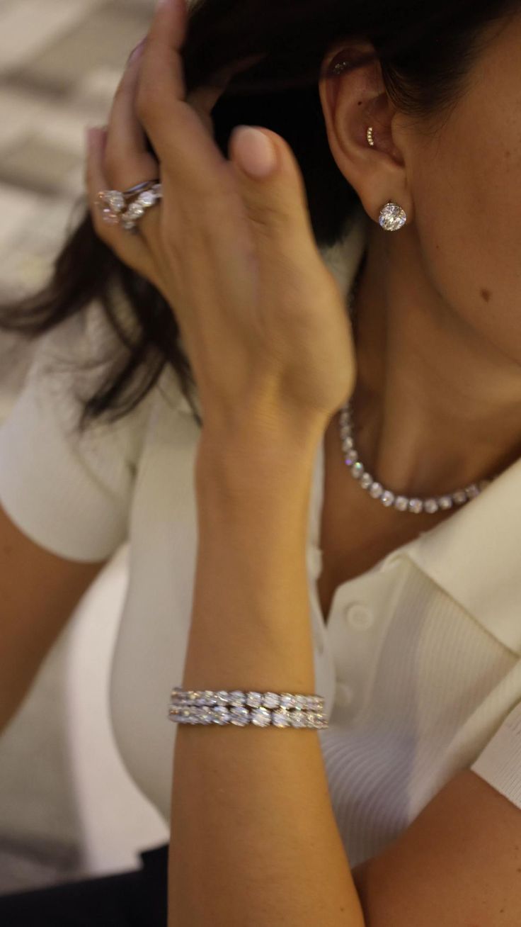 Model in a white knit top wearing a diamond line necklace, round diamond studs, stacked diamond rings and a diamond tennis bracelet