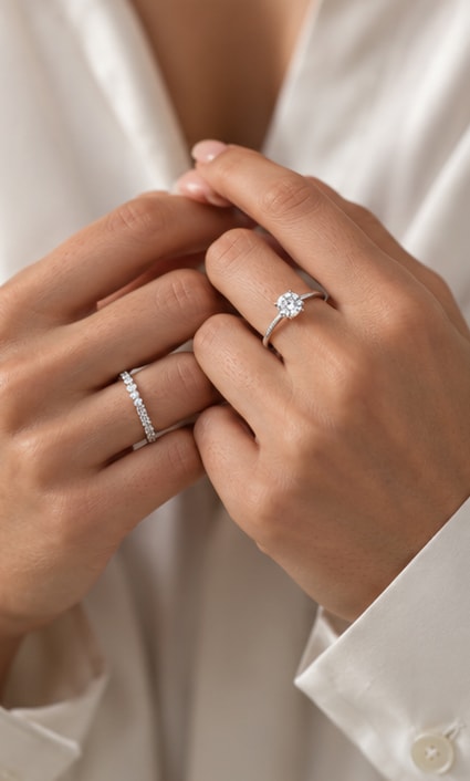 Hands wearing a round diamond solitaire ring and a diamond eternity band