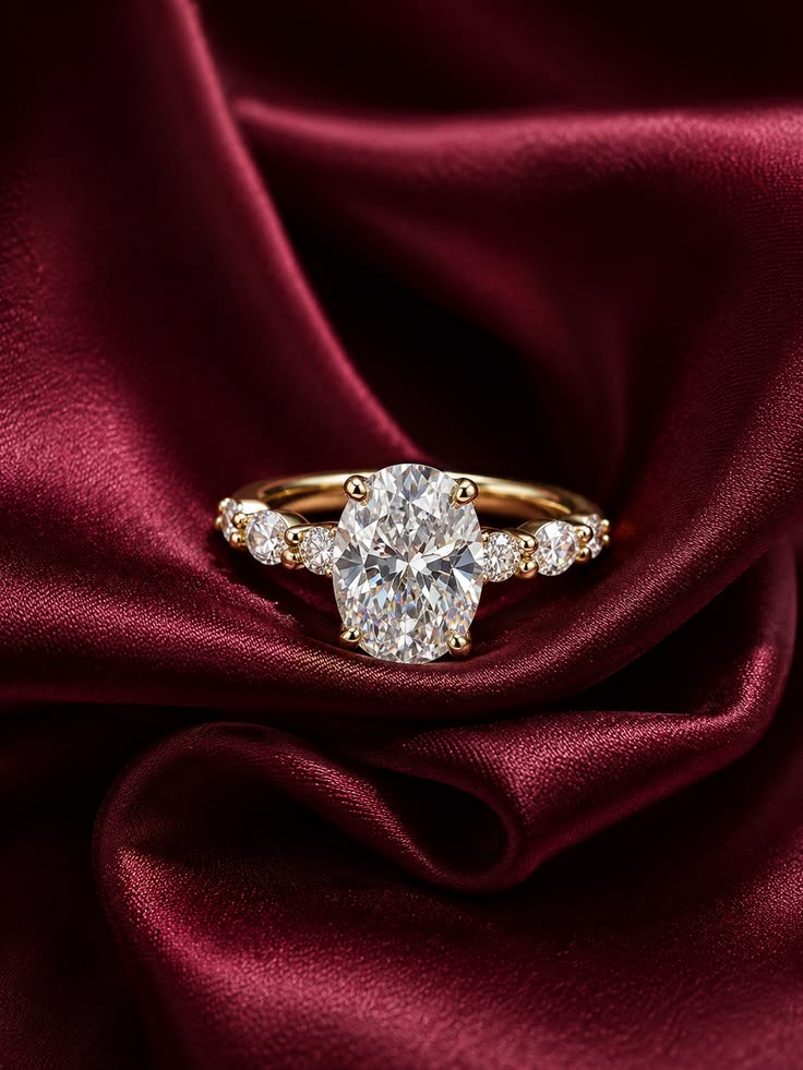 Oval diamond ring with side stones on deep red satin